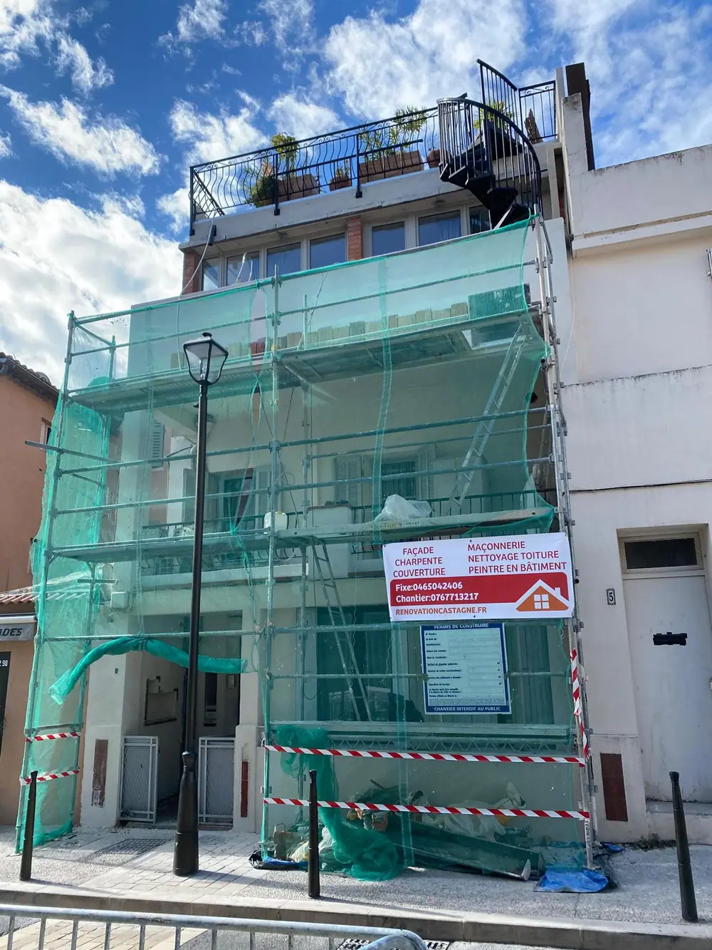 Chantier de façade en rue, échafaudage ceinturé d'un filet et barrières au pied — Castagne Couverture