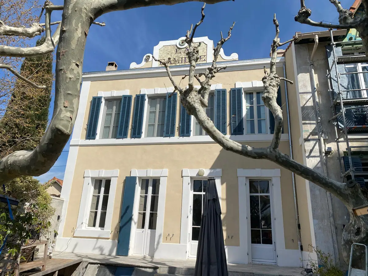 Bastide ancienne ravalée, enduit ocre clair, encadrements repris en blanc, volets bleus