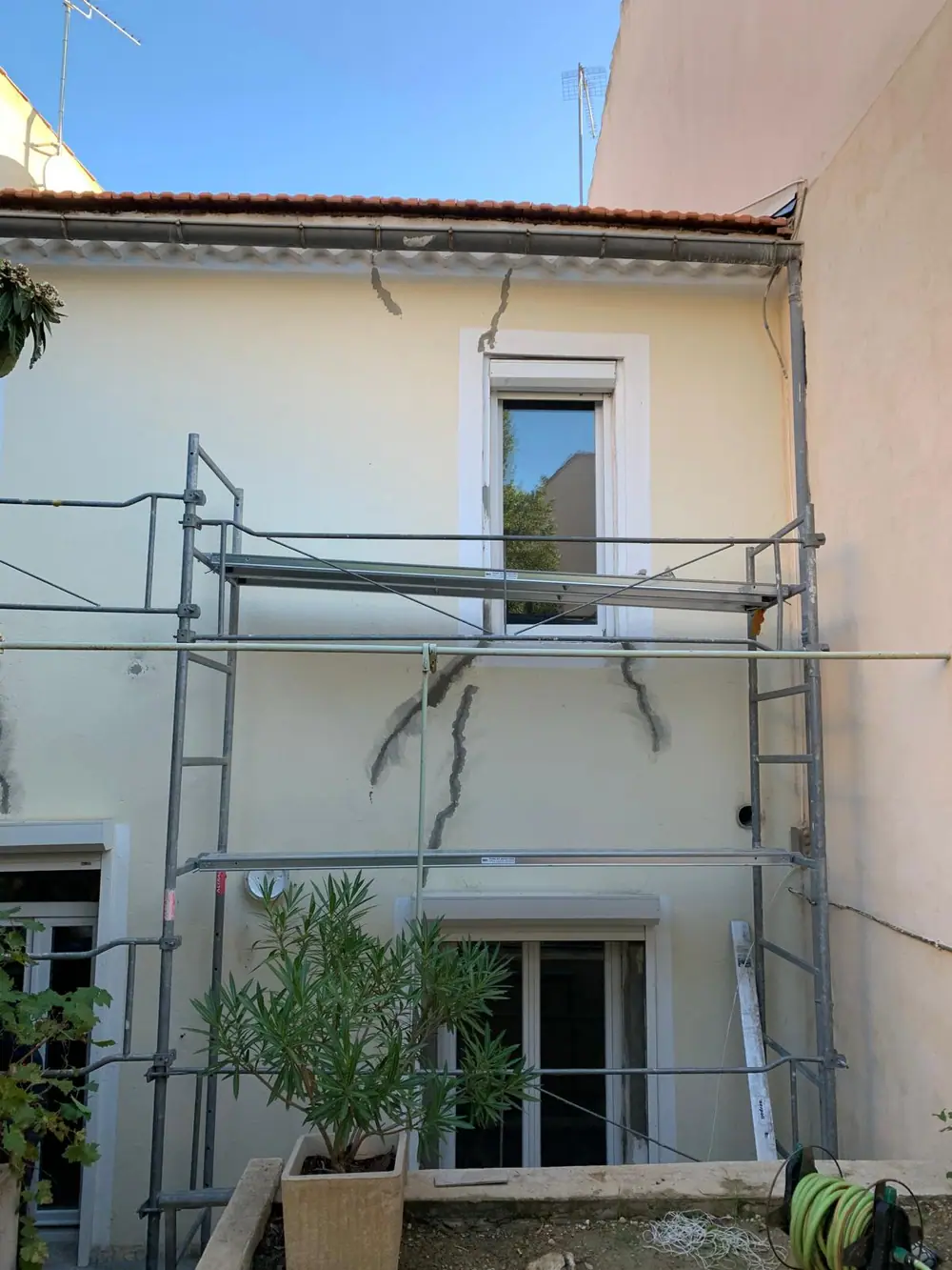 Fissures en escalier ouvertes et pontées au mortier de réparation sur une façade sous échafaudage